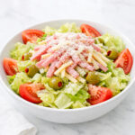 1905 salad with iceberg lettuce, ham, Swiss cheese, tomatoes, and olives in a white bowl