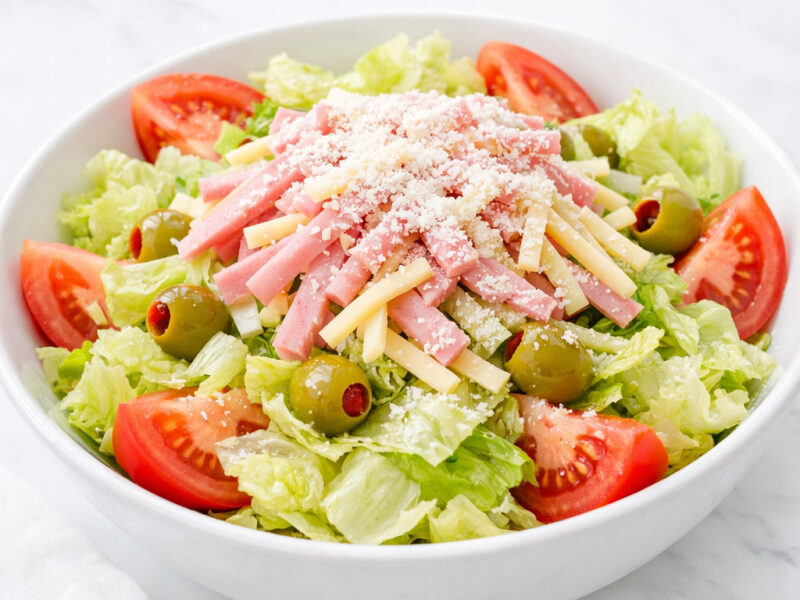 1905 salad with iceberg lettuce, ham, Swiss cheese, tomatoes, and olives in a white bowl