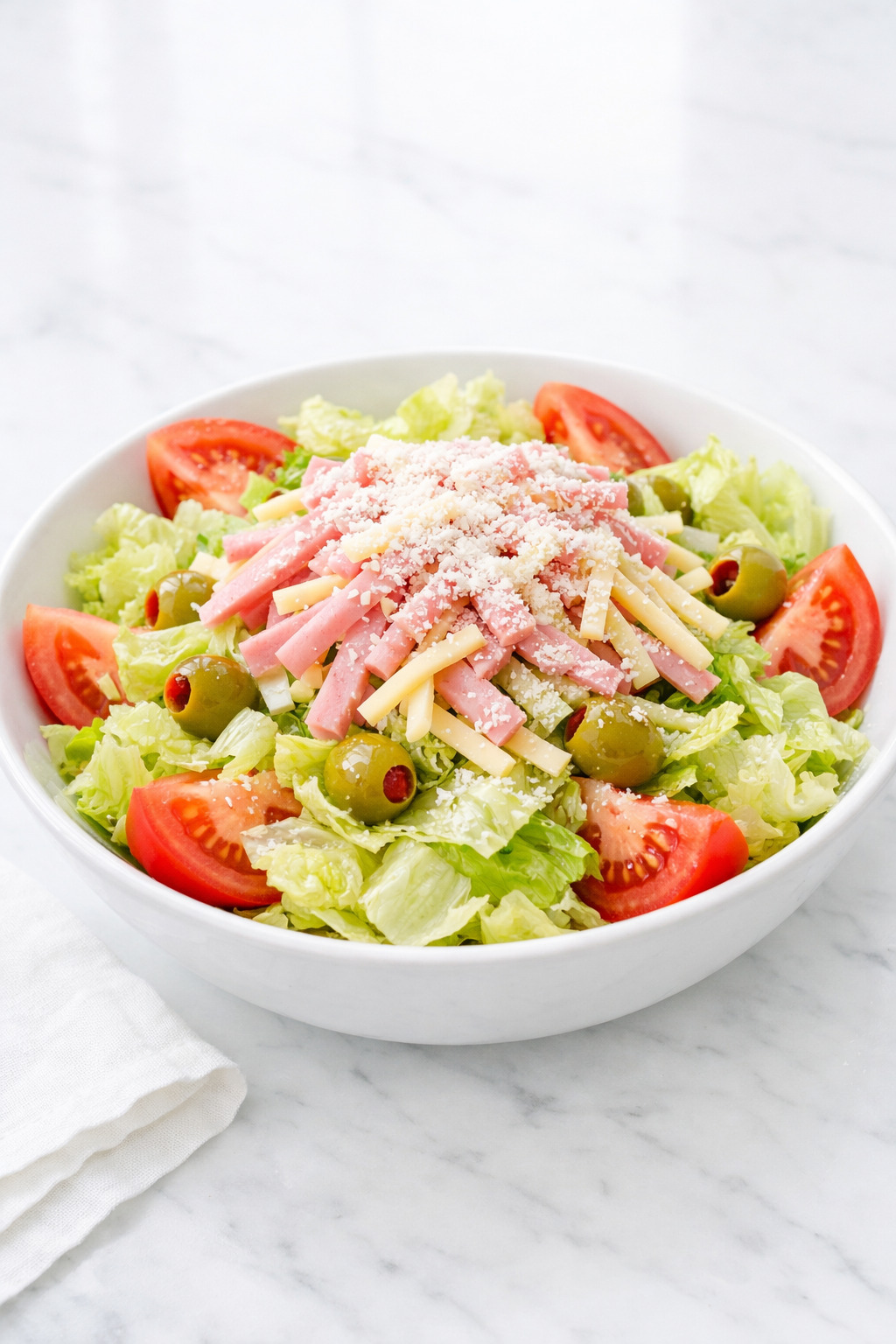 1905 salad with iceberg lettuce, ham, Swiss cheese, tomatoes, and olives in a white bowl
