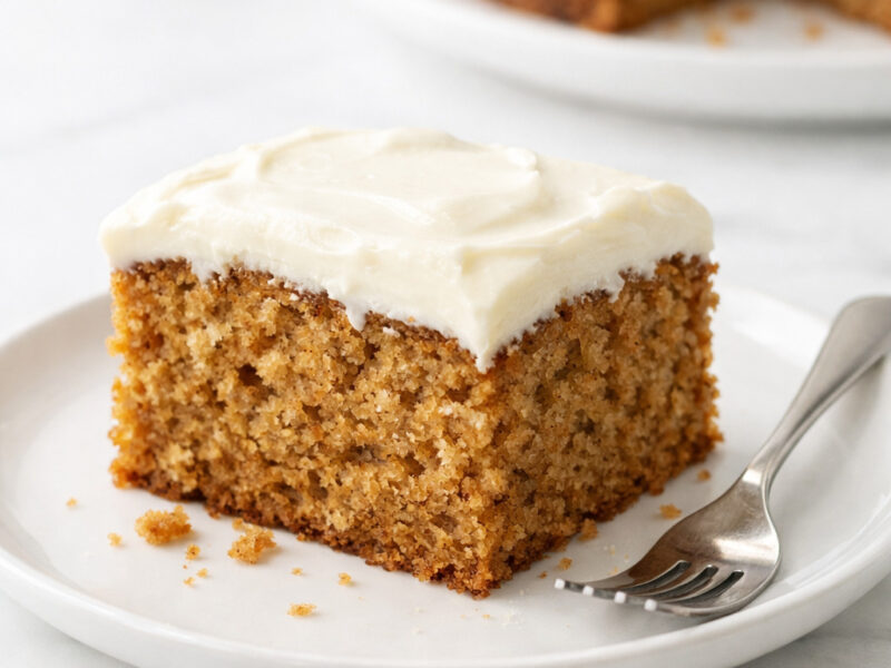 Applesauce cake slice with cream cheese frosting on a white plate