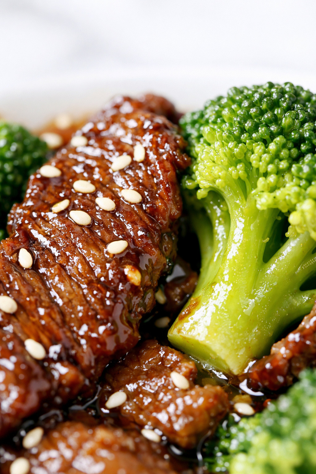 Close-up of glossy sauced beef slices with broccoli florets and sesame seeds