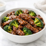 Beef and broccoli stir fry with glossy garlic soy sauce and sesame seeds in a white ceramic bowl