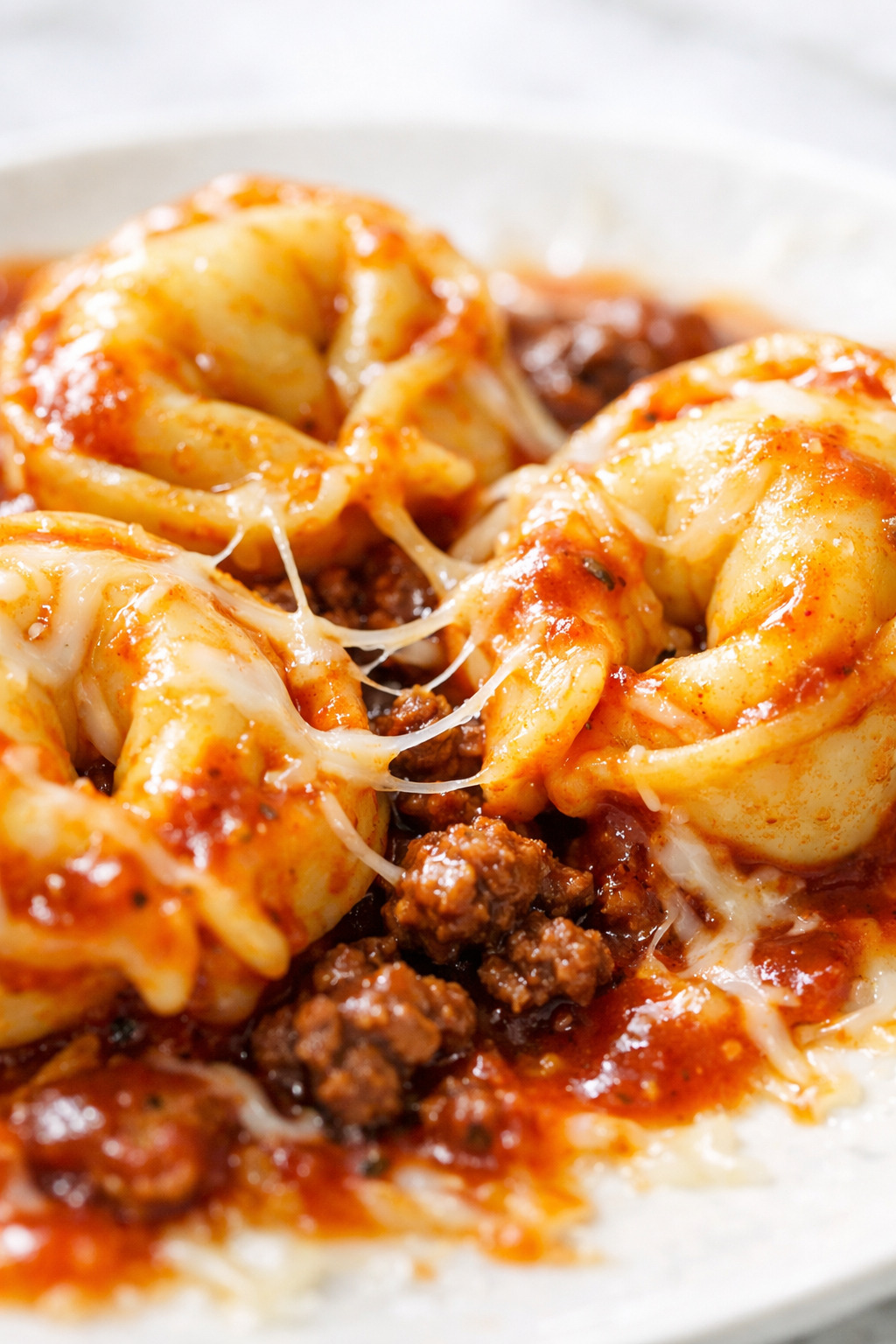 Close-up of tortellini coated in enchilada sauce with stretchy melted cheese