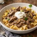 A bowl of beef stroganoff with tender beef strips in creamy mushroom sauce over egg noodles