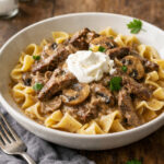 A bowl of beef stroganoff with tender beef strips in creamy mushroom sauce over egg noodles