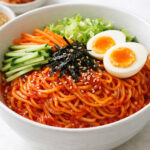 Bowl of Korean bibimmyeon with colorful vegetables and soft-boiled egg