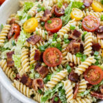 A large white bowl filled with BLT pasta salad with rotini pasta, crispy bacon, cherry tomatoes, romaine lettuce, and creamy ranch dressing