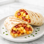 Breakfast wraps with scrambled eggs, bacon, and melted cheese cut in half on a white plate