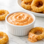 Homemade Burger King zesty sauce in a white ramekin with onion rings and fries