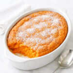 Golden brown carrot souffle in a white baking dish with a puffed caramelized top