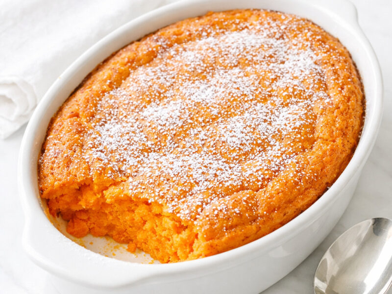 Golden brown carrot souffle in a white baking dish with a puffed caramelized top
