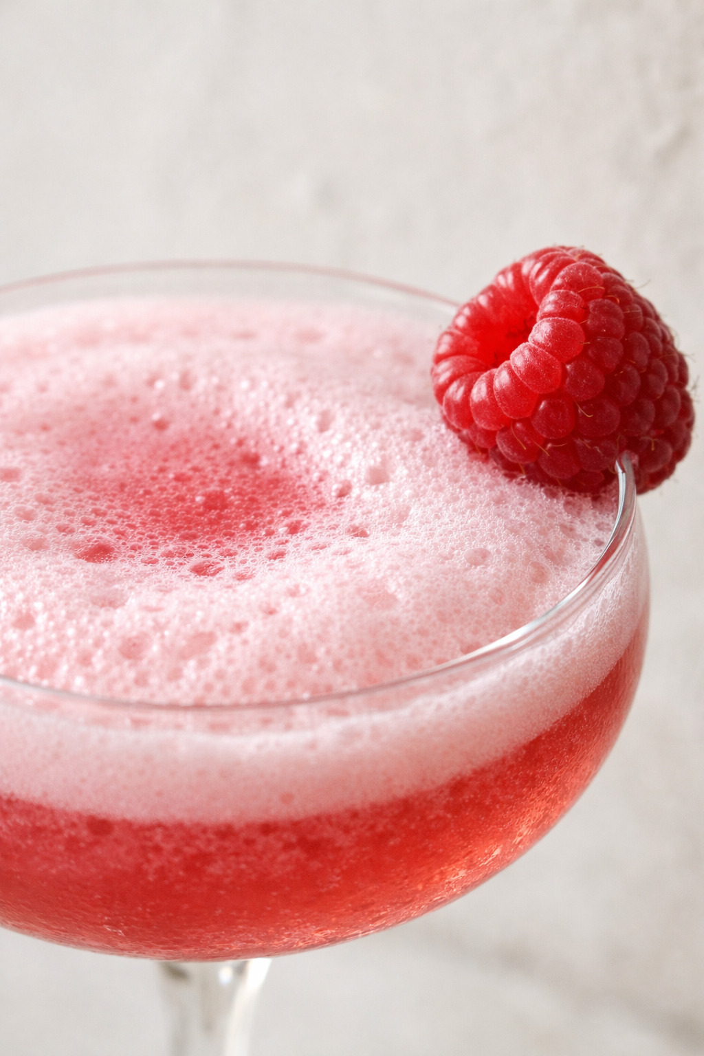 Closeup of frothy pink Clover Club Cocktail with raspberry garnish