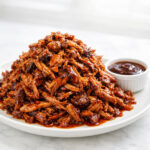 Coca cola pulled pork piled high on a white plate with BBQ sauce