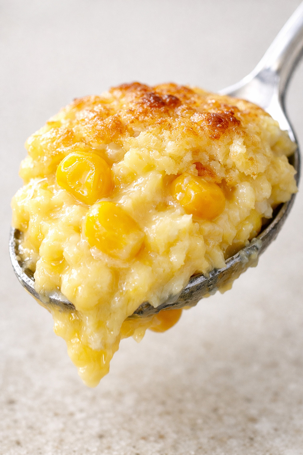 Extreme closeup of a spoonful of corn pudding showing golden custardy interior with visible corn kernels