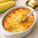 Corn pudding in a white ceramic oval baking dish on light concrete