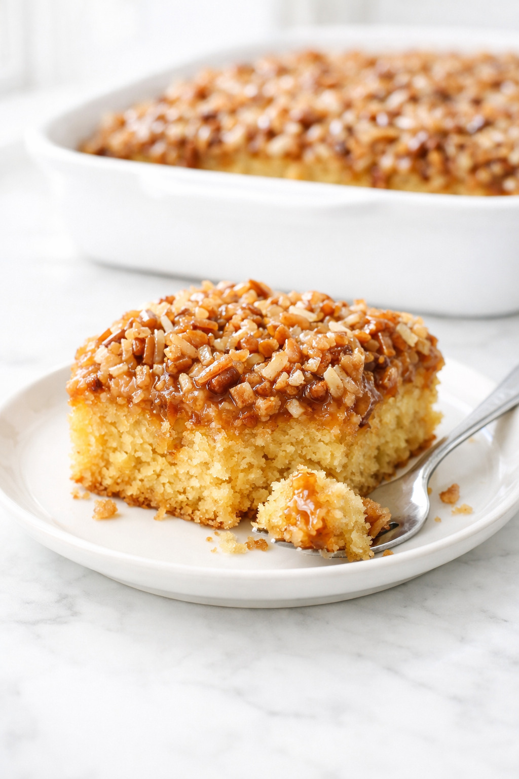 Slice of do nothing cake on white plate showing moist crumb and coconut pecan topping