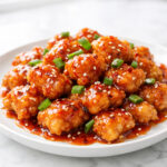 Firecracker chicken pieces glazed with sweet and spicy sauce on a white plate