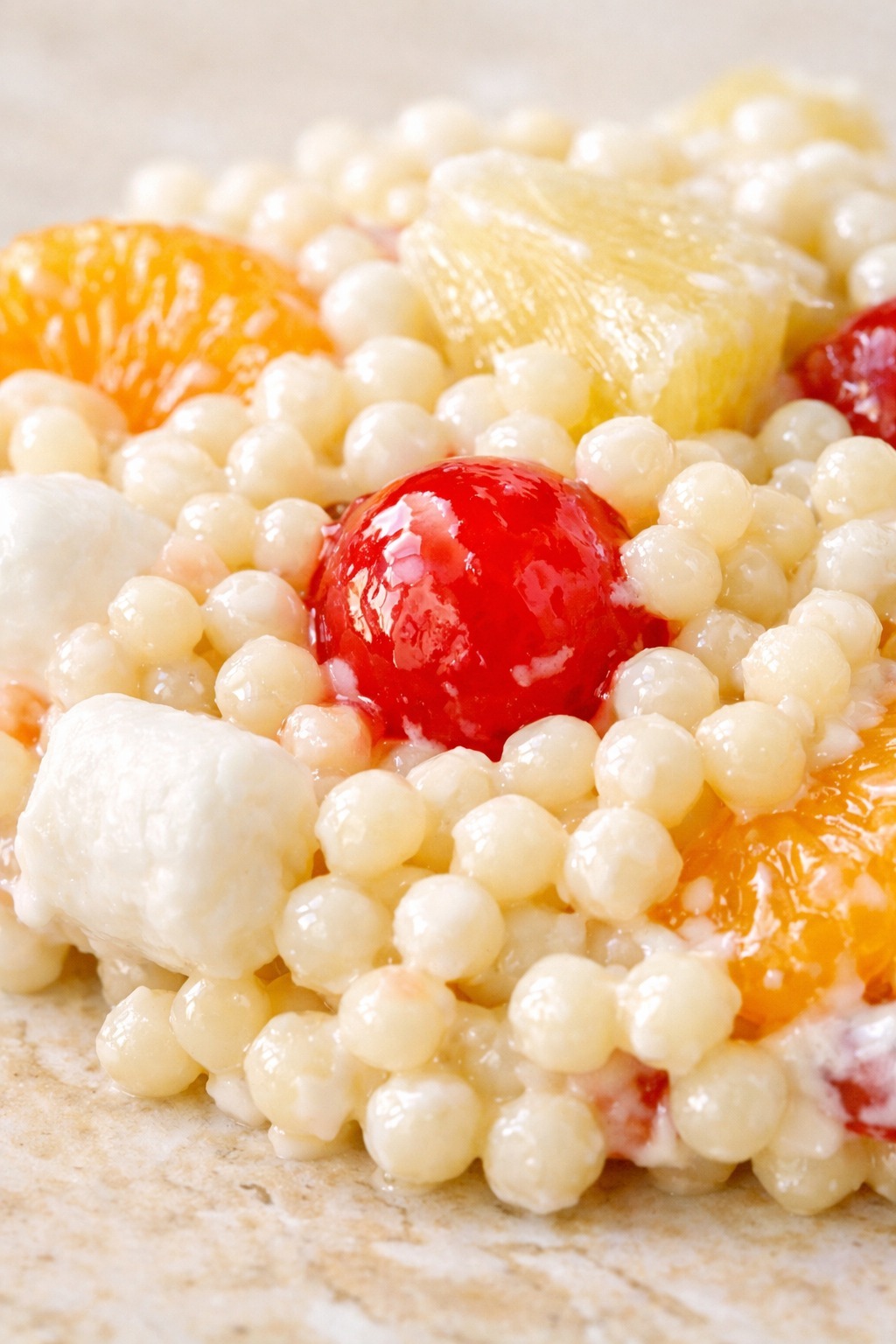 Extreme closeup of Frog Eye Salad showing acini de pepe pasta pearls coated in creamy dressing with mandarin orange segments and maraschino cherries