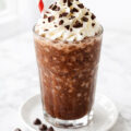 Frozen hot chocolate in a tall glass topped with whipped cream and chocolate shavings