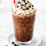 Frozen hot chocolate in a tall glass topped with whipped cream and chocolate shavings