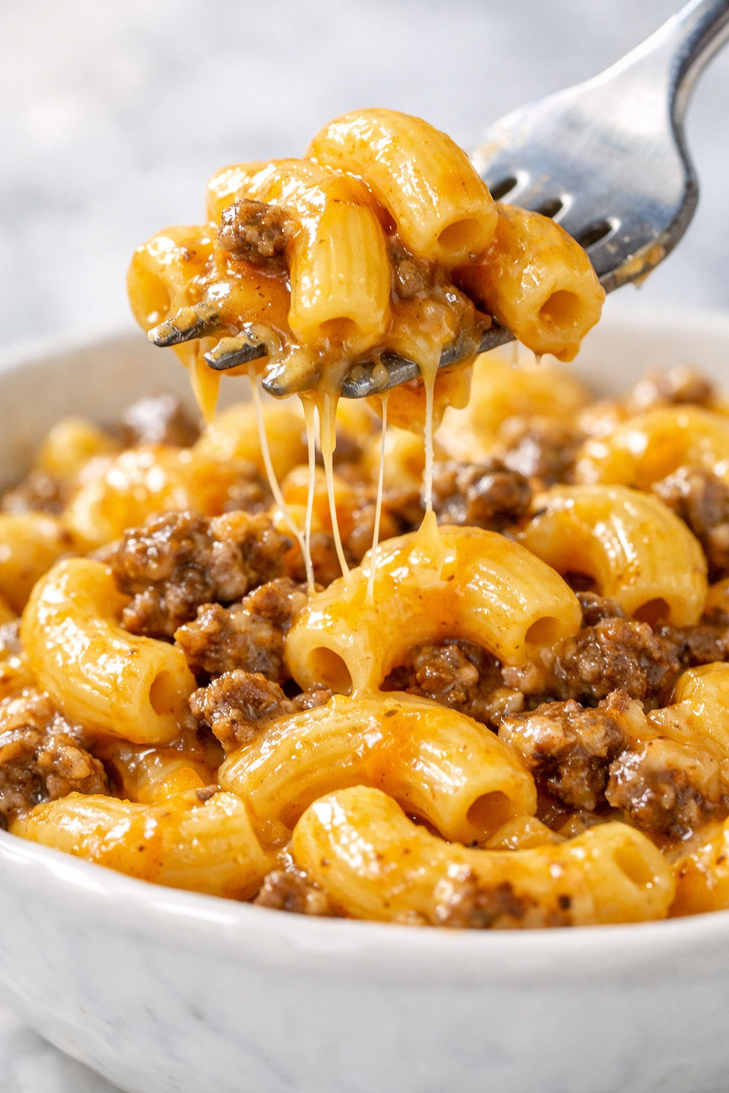 Close-up of elbow macaroni coated in thick golden cheddar cheese sauce with ground beef