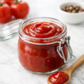 Homemade ketchup in a glass jar on white marble