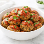 Keto meatballs in a white bowl topped with marinara sauce and fresh parsley