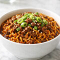 Korean style ground beef ramen in white bowl with gochujang sauce green onions and sesame seeds