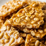 Golden shards of microwave peanut brittle loaded with roasted peanuts on a white ceramic plate