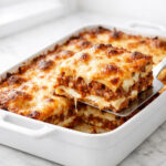 Baked ragu lasagna in a white ceramic baking dish with golden bubbly cheese on top