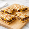Smashburger quesadillas with melted cheese and crispy beef on a cutting board