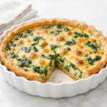 Golden brown spinach quiche in a white fluted ceramic dish with one slice cut