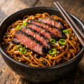 Bowl of sticky beef noodles with caramelized beef and glossy brown sauce
