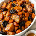 Tzimmes in a white baking dish with honey-glazed sweet potatoes, carrots, and prunes