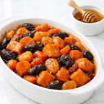 Tzimmes in a white baking dish with honey-glazed sweet potatoes, carrots, and prunes