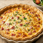 Ham and cheese quiche in a white pie dish with golden top